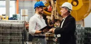 Ejecutivos de ventas industriales dentro de una fábrica cierran acuerdo de ventas con un apretón de manos. Base 3 Crecimiento Digital B2B.